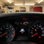 Injection à contrôler : quel budget prévoir pour éviter une grosse panne Gros plan réaliste du tableau de bord d’une voiture avec un voyant moteur allumé, dans un garage en arrière-plan flou, ambiance d’information automobile.