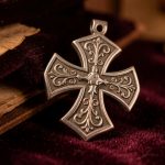 Croix des Templiers sur un bijou : reconnaître le symbole et son histoire Pendentif en argent orné d’une croix pattée, posé sur un velours sombre à côté d’un parchemin ancien dans une ambiance historique.