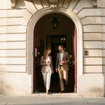 Comment préparer sa visite au Musée du Vin de Paris et choisir sa dégustation ? Entrée élégante et discrète d’un musée du vin parisien, avec une femme et un homme arrivant sous la lumière chaude de la fin d’après-midi.