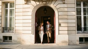 Entrée élégante et discrète d’un musée du vin parisien, avec une femme et un homme arrivant sous la lumière chaude de la fin d’après-midi.