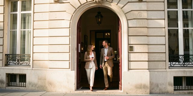 Entrée élégante et discrète d’un musée du vin parisien, avec une femme et un homme arrivant sous la lumière chaude de la fin d’après-midi.