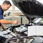 Quand faut-il prévoir l’entretien auto selon le kilométrage ? Un mécanicien contrôle le niveau d’huile d’une voiture familiale dans un atelier lumineux, avec un carnet d’entretien ouvert sur le capot.