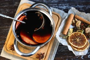 Casserole de vin rouge avec bâtons de cannelle, étoiles de badiane et rondelles d’orange pour préparer un vin chaud parfumé.