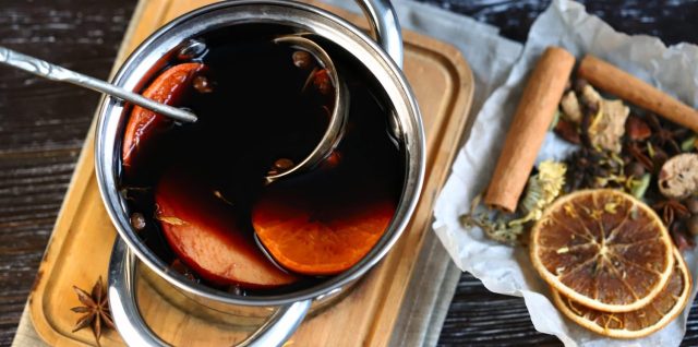 Casserole de vin rouge avec bâtons de cannelle, étoiles de badiane et rondelles d’orange pour préparer un vin chaud parfumé.