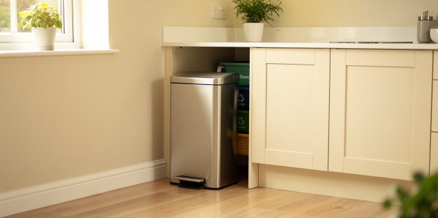Cuisine familiale lumineuse et contemporaine avec une poubelle à pédale en inox près du plan de travail et des bacs de tri discrets.